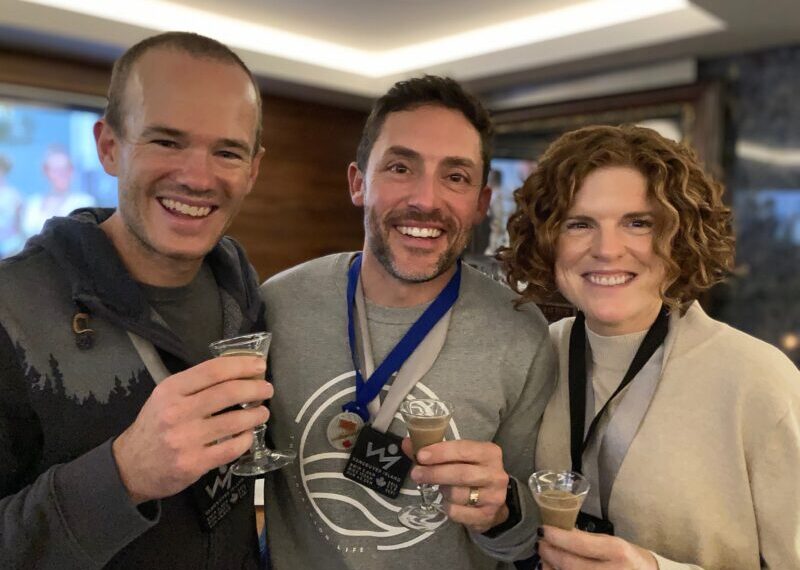 Three people smiling while holding glasses of wine.