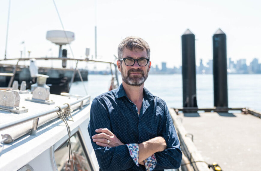 A man standing on a boat in front of a city.
