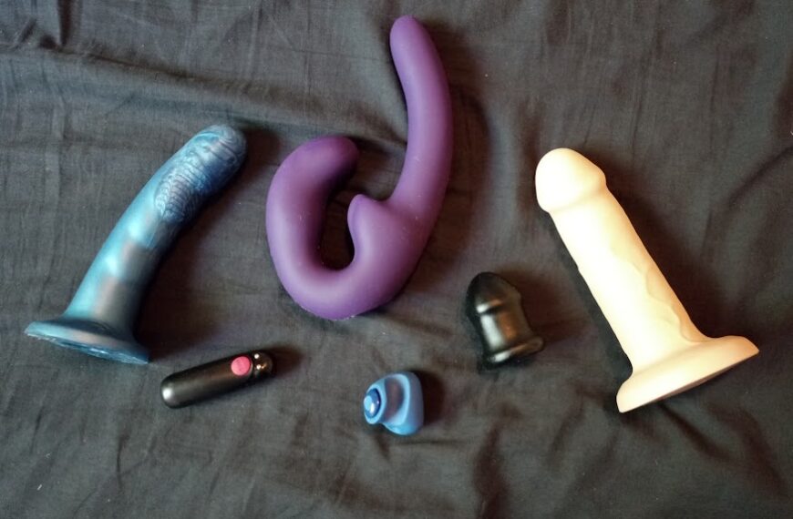 A group of different types of dildos laying on a bed.