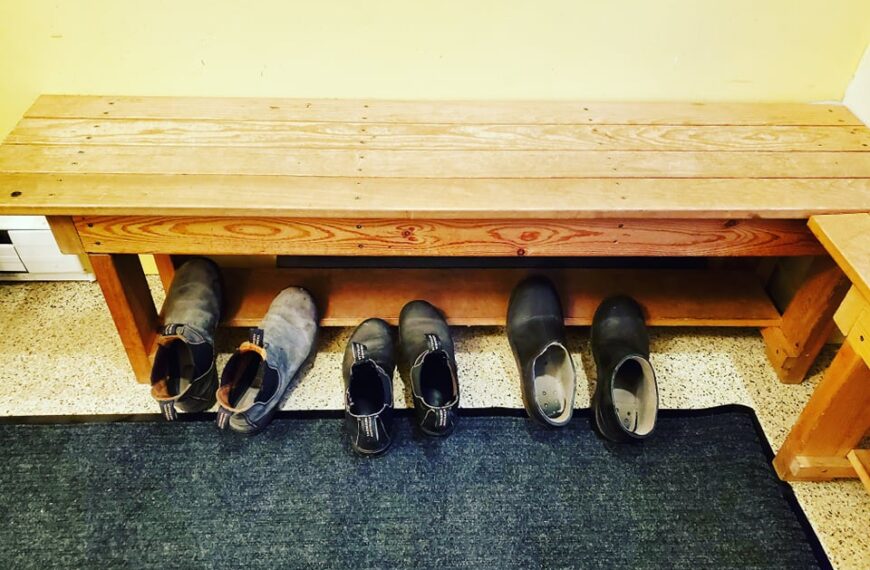 A wooden bench with several pairs of shoes on it.