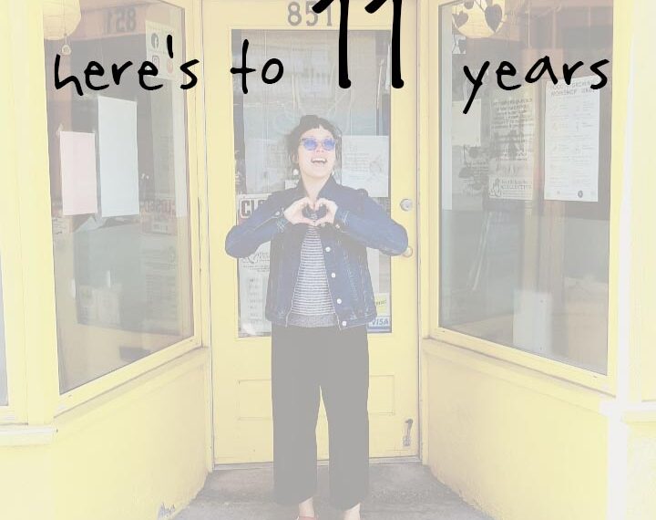 A woman standing in front of a yellow door with the words here's to 11 years.