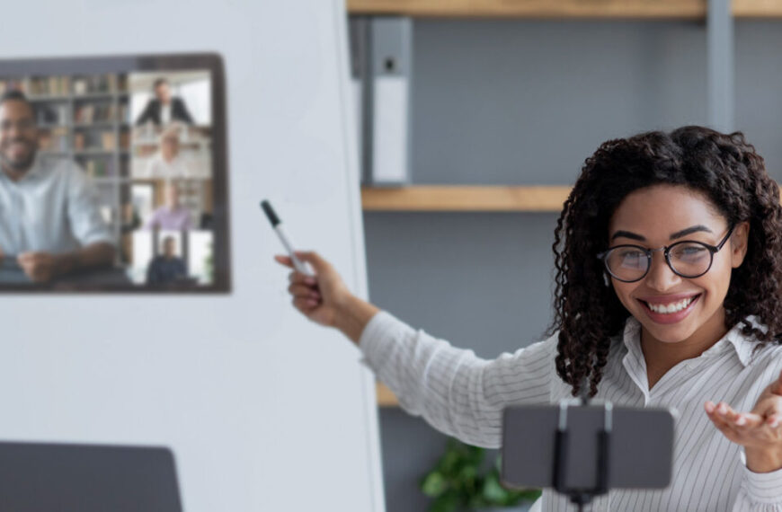 A woman is pointing to a video screen in front of a whiteboard.