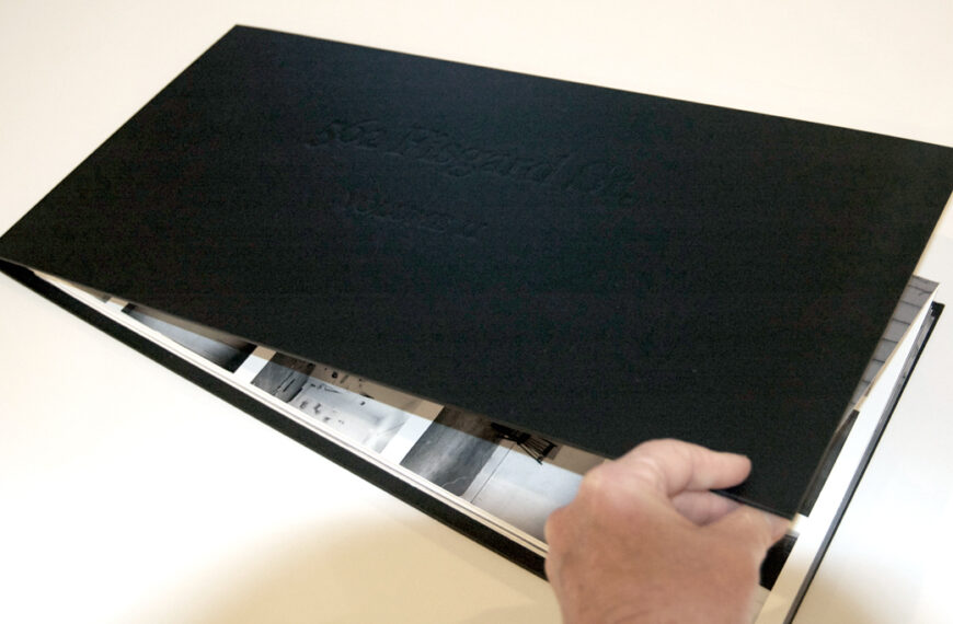 A person opening a black book on a table.