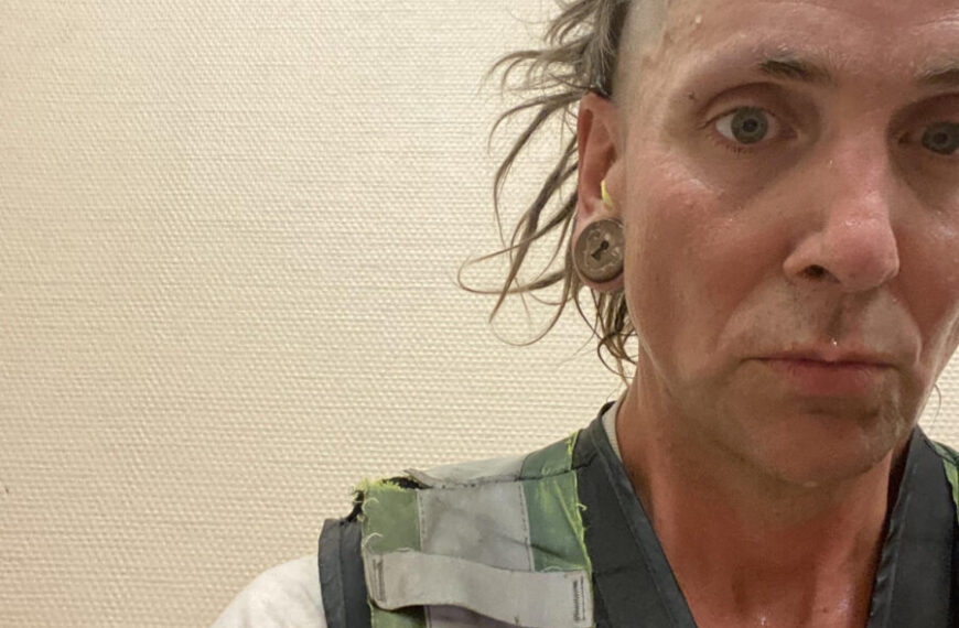 A man in a vest with a shaved head.