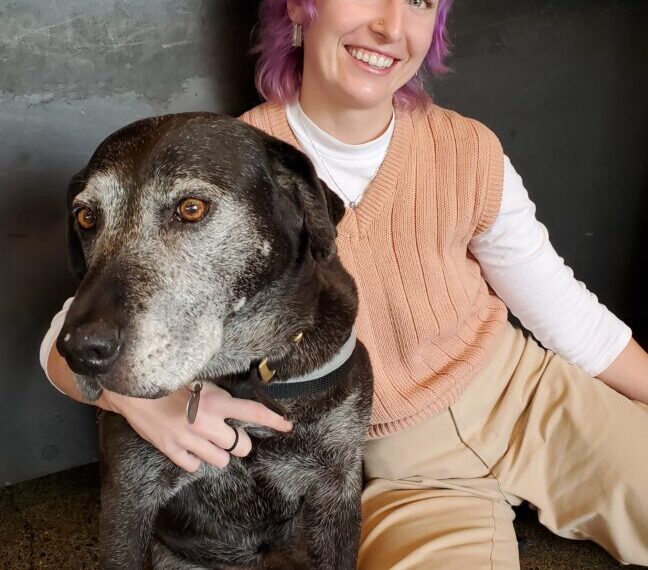 A woman with purple hair and a black dog.