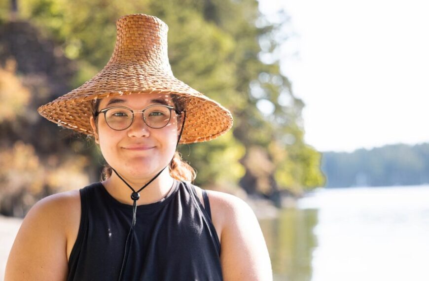 A woman wearing glasses and a straw hat in front of a body of water.