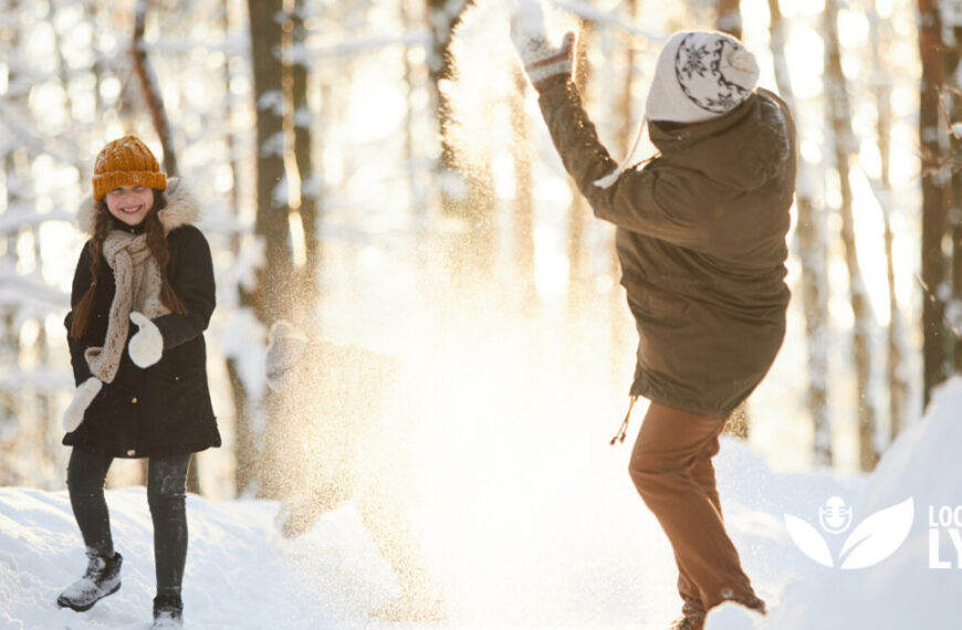Two people playing in the snow in a wooded area.