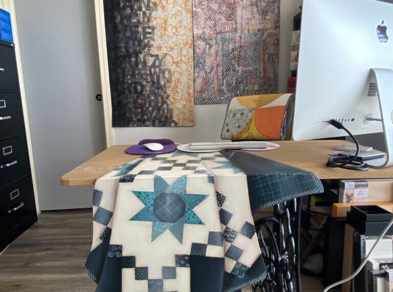 A quilt sitting on a desk in a home office.