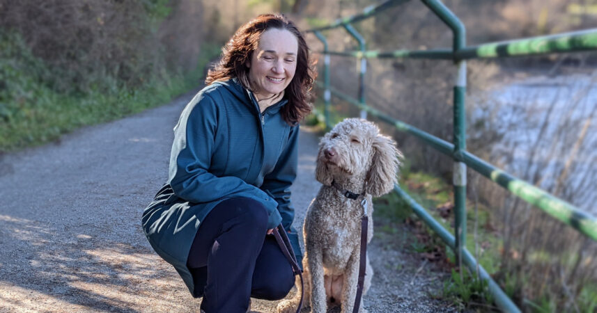 A woman crouching down next to a river with her dog.