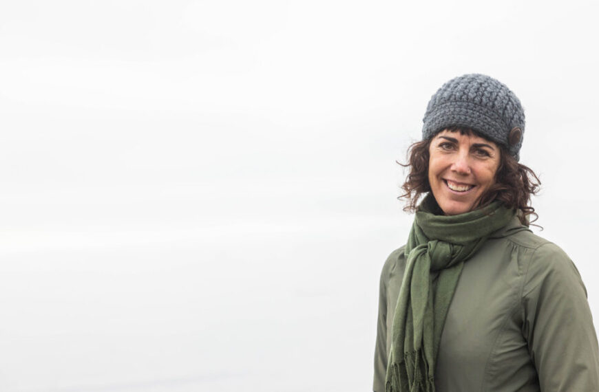 A woman wearing a hat and scarf standing on a beach.