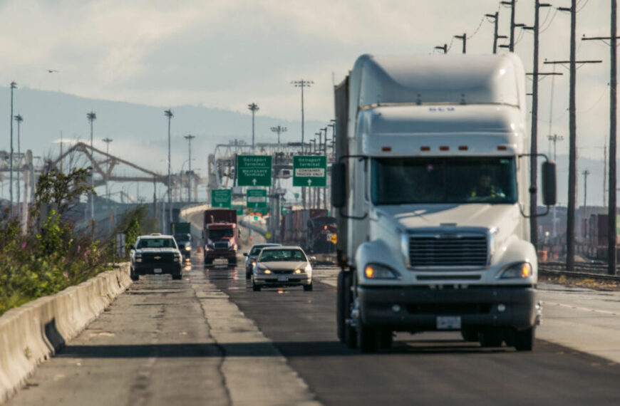 A semi truck driving down a highway with cars in the background.