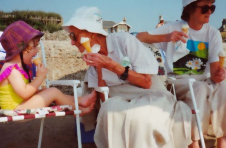 A woman and a child eating ice cream on the beach.
