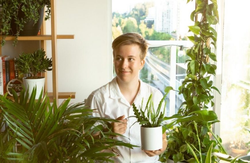 A woman holding a potted plant in front of a window.