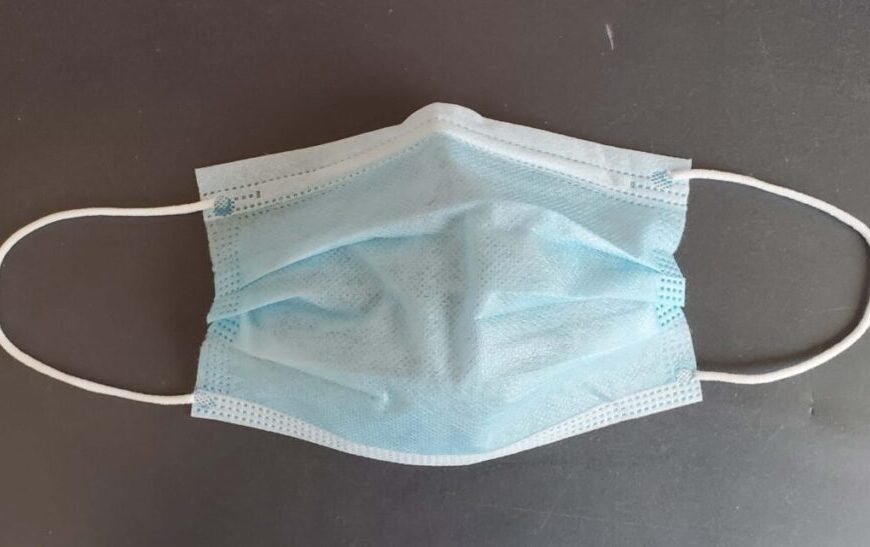 A blue surgical face mask on a dark surface.