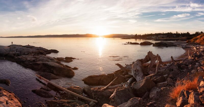 The sun is setting over a rocky shoreline.