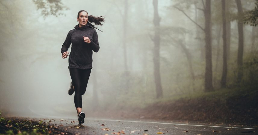 A woman jogging in a foggy forest.