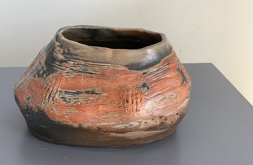 An orange and brown ceramic vase sitting on a table.