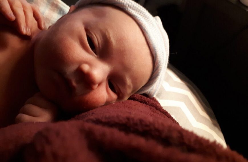 A baby is laying on a blanket with a hat on.