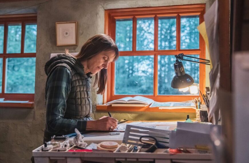 A woman writing at her desk in front of a window.