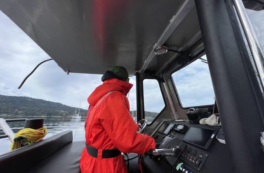 A man in a red jacket is sitting in the steering wheel of a boat.