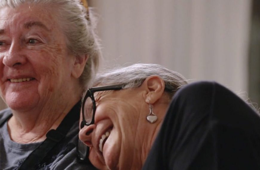 Two women are laughing while sitting next to each other.