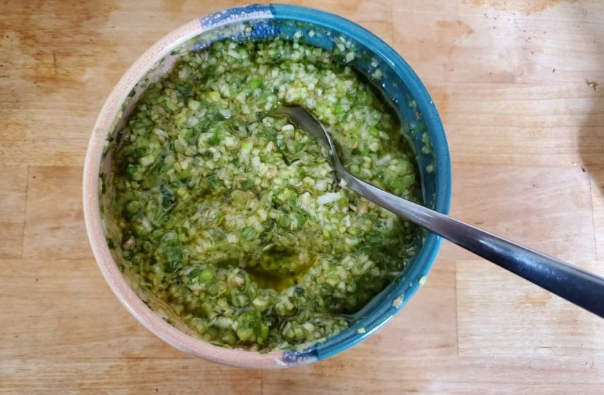 A bowl of green pesto on a wooden table.