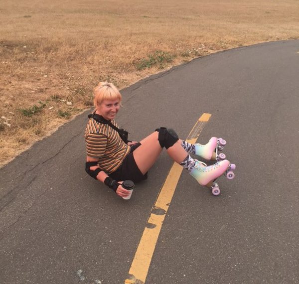 A girl sitting on a skateboard in a field.