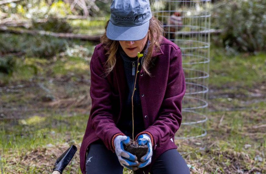 A woman is kneeling down in the woods.