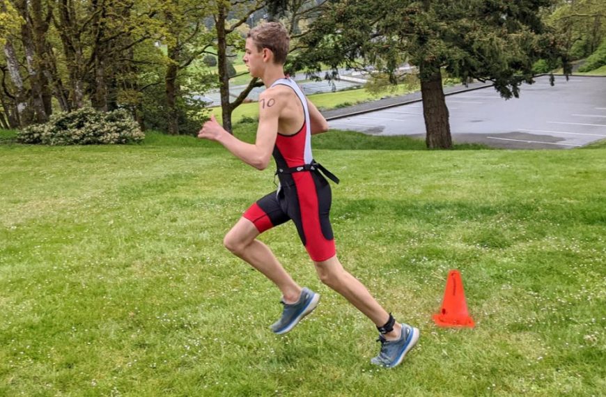 A young man running in a park with cones in the background.