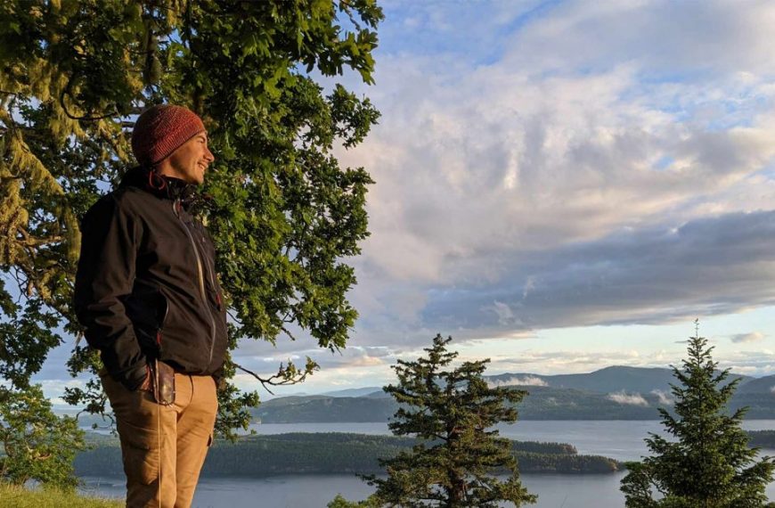 A man standing on a hill overlooking a lake.