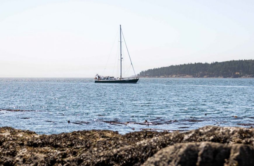 A sailboat sails in the ocean near rocky shores.