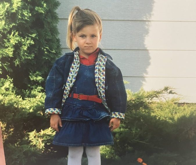 A little girl in a blue dress standing in front of a house.