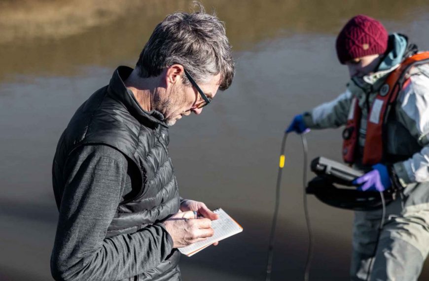 Two people standing next to a river looking at a notepad.