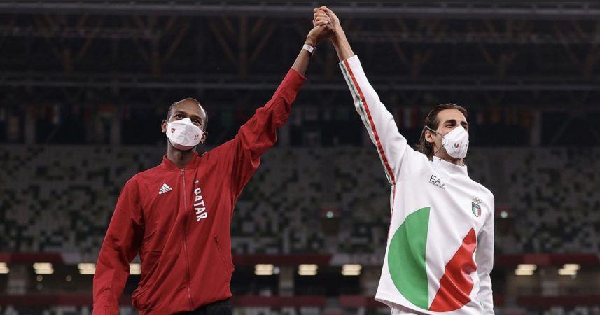 Two men in face masks standing next to each other on a soccer field.