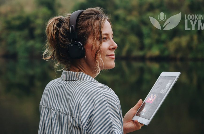 A woman wearing headphones is holding an ipad near a body of water.