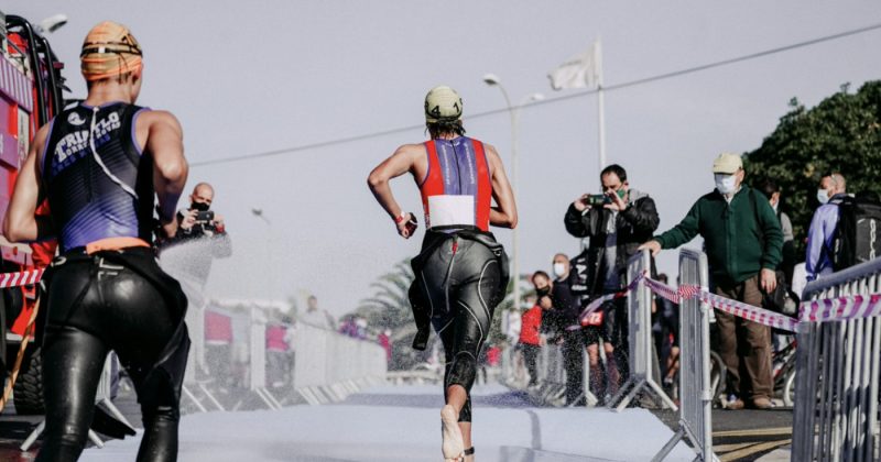 Two triathletes running on a track in front of spectators.