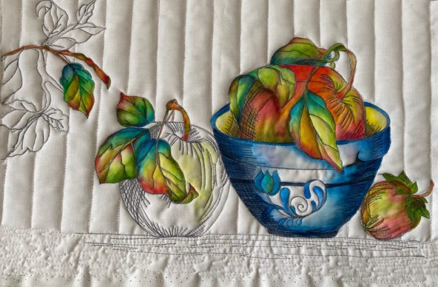 A quilt with a bowl of apples and leaves.