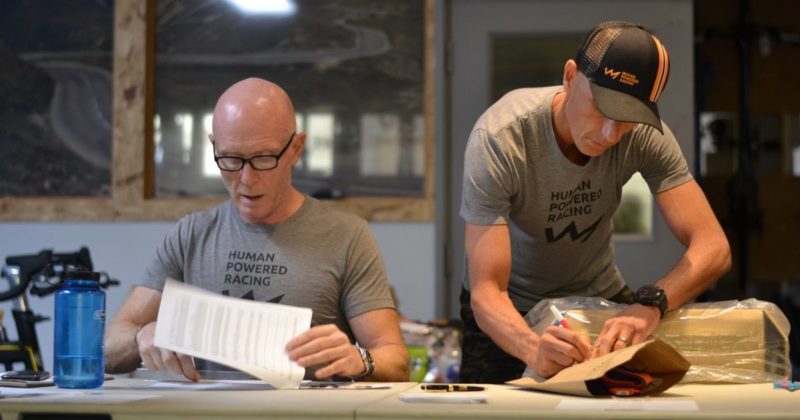 Two men sitting at a table with paper and pens.