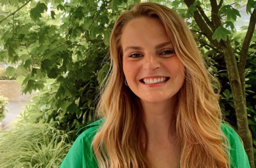A woman in a green shirt smiling in front of trees.