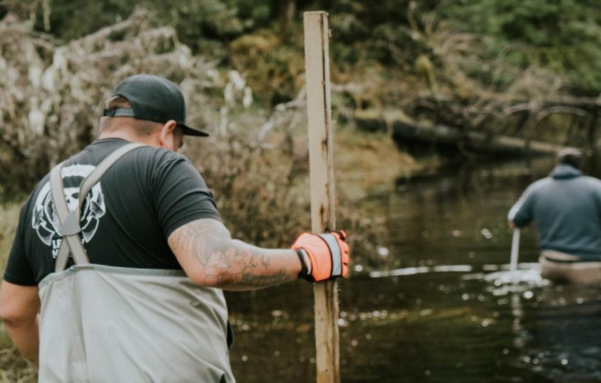 Two men standing in a river with sticks in their hands.