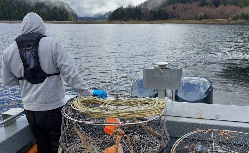A man in a hoodie is holding a fishing net on a boat.