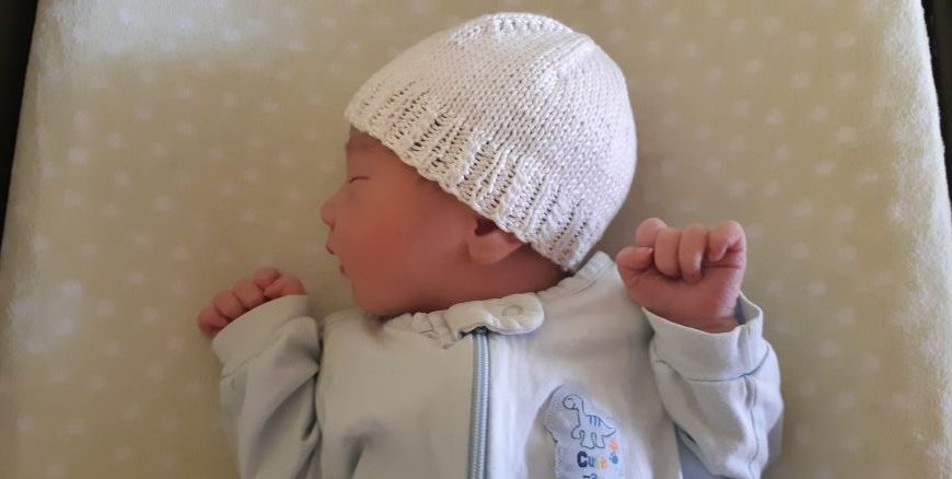 A baby sleeping in a white knitted hat.