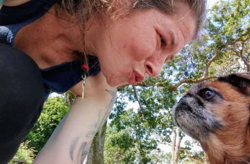 A woman kissing a dog with tattoos.