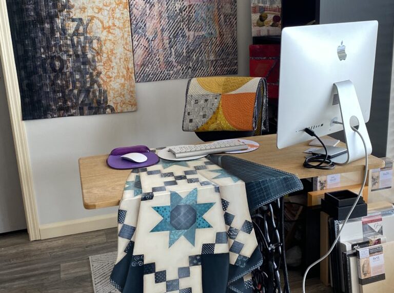 A desk with a computer and a quilt on it.