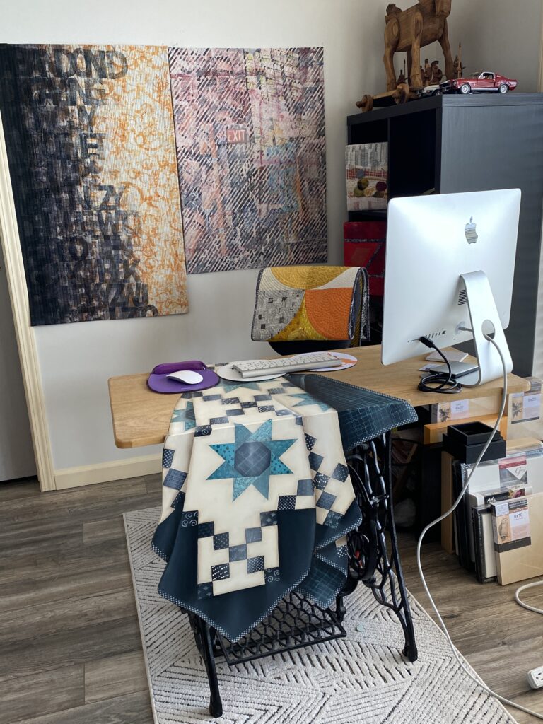 A desk with a computer and a quilt on it.