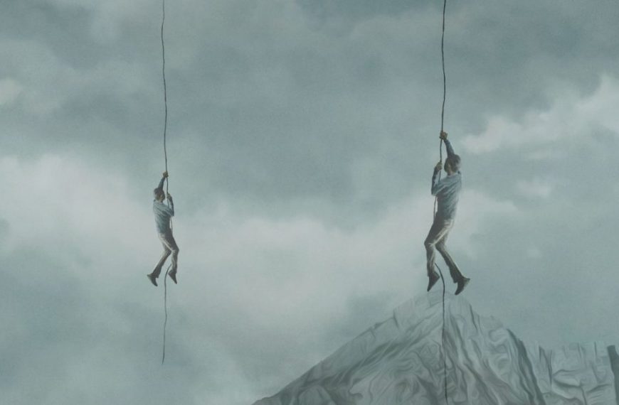 Two people hanging from ropes on a mountain.