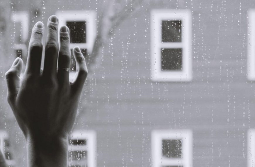 A black and white photo of a hand reaching out of a window.
