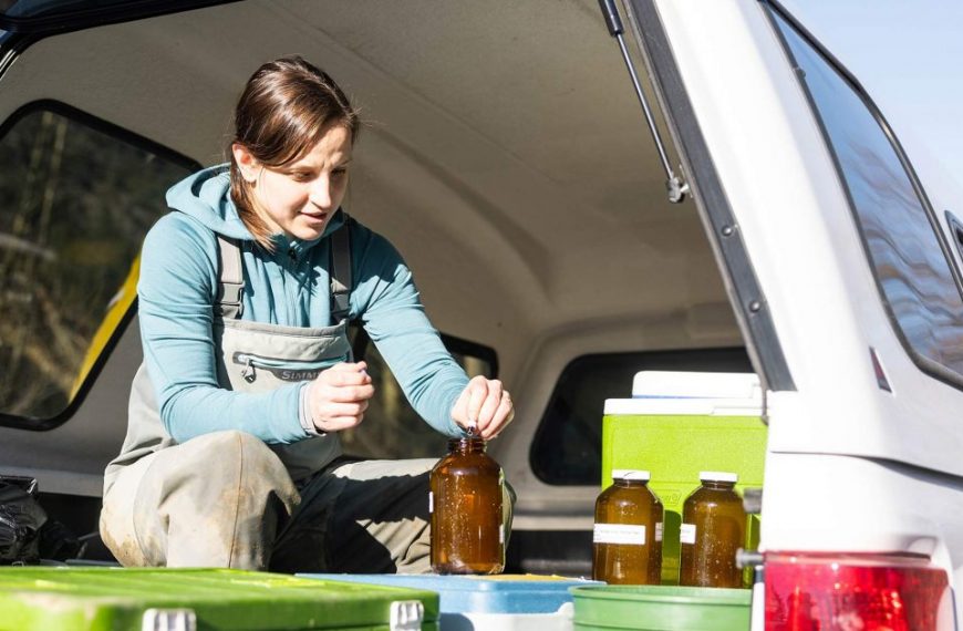 A woman in overalls sitting in the back of a truck.