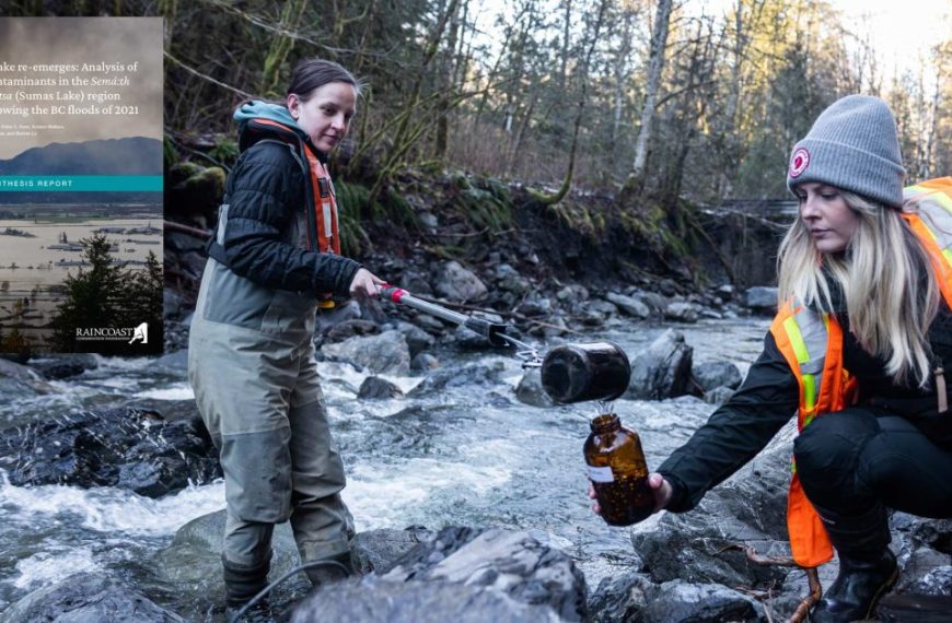 Two women kneeling down next to a river with a bottle in their hands.