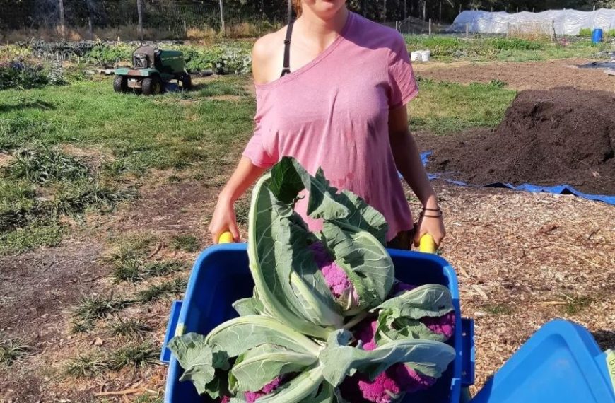A woman standing in front of a pile of cabbages.